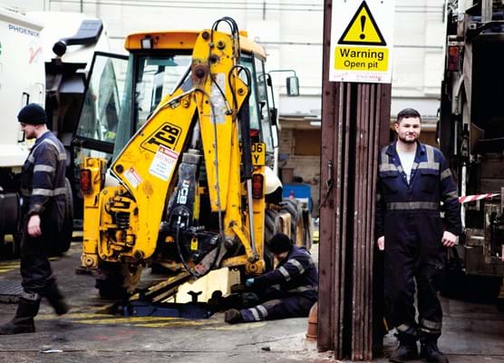 small yellow JCB in a garage with 2 male workmen