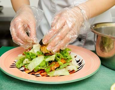 close up of person wearing plastic gloves plating up a salad on a plate