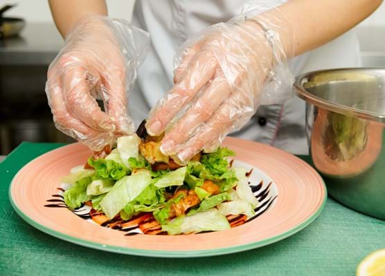 close up of person wearing plastic gloves plating up a salad on a plate